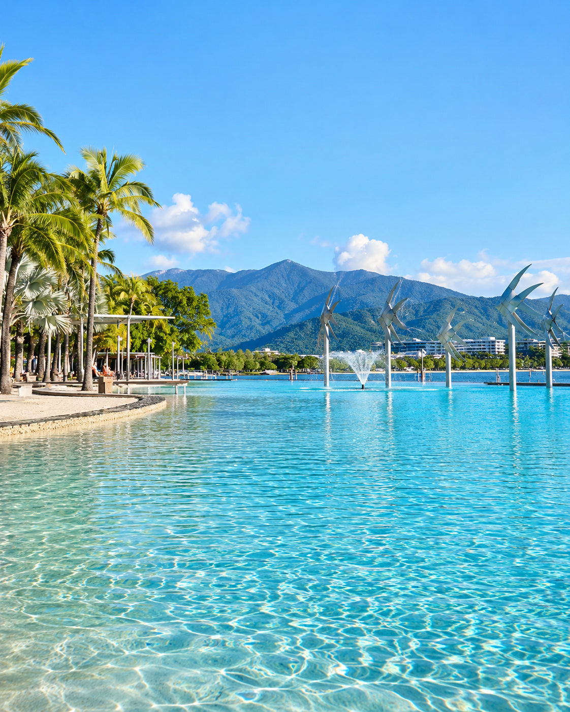 Cairns: cairns Esplanade Lagoon and waterfront with tropical palms, blue water and green mountains in bright sunny daylight