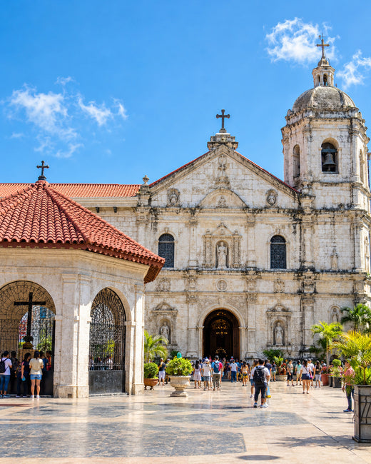 Cebu: Steinfassade und Glockenturm der Basilika Santo Niño mit tropischem Garten im Sonnenschein