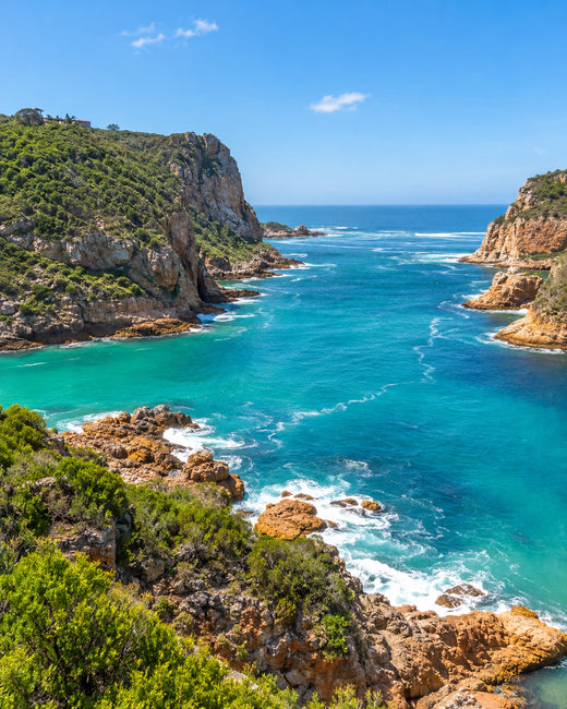 Knysna: Sandsteinfelsen der Knysna Heads am Eingang einer türkisfarbenen Lagune mit grünen Hängen