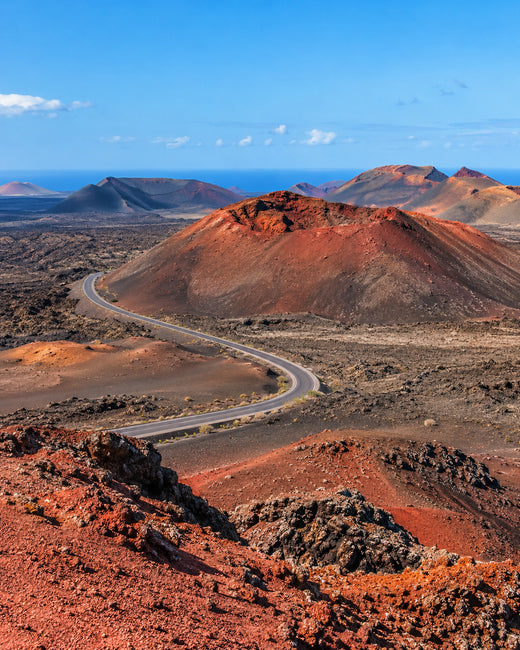 Lanzarote: Vulkankegel von Timanfaya mit rot-schwarzen Lavafeldern und kurviger Straße unter blauem Himmel