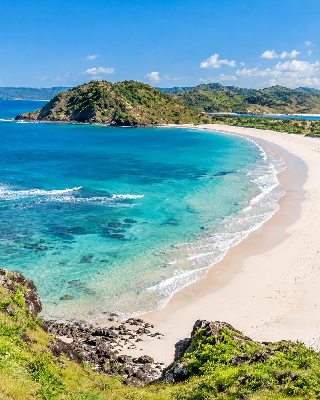 Lombok: turkusowa zatoka Tanjung Aan, jasna łukowata plaża i zielone nadmorskie wzgórza w słońcu