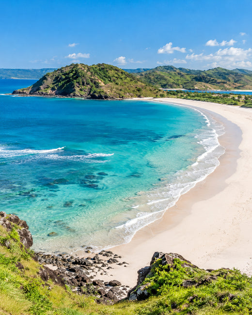 Lombok: türkisfarbene Tanjung-Aan-Bucht mit hellem Sandbogen und grünen Küstenhügeln im Sonnenschein