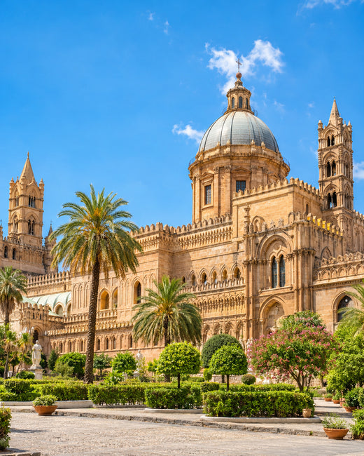 Palermo: helle Steinfassade der Kathedrale von Palermo mit verzierten Türmen und Palmen unter blauem Himmel
