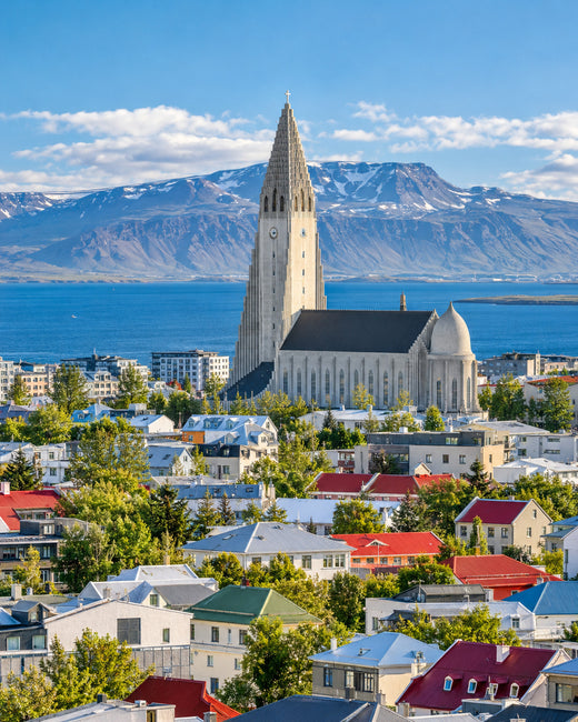 Reykjavík: Hallgrímskirkja über bunten Dächern von Reykjavík mit blauem Meer und Bergen im Hintergrund