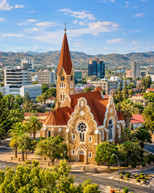 Windhoek: Sandsteinmauern und rotes Dach der Christuskirche mit modernen Stadtgebäuden und grünen Hügeln