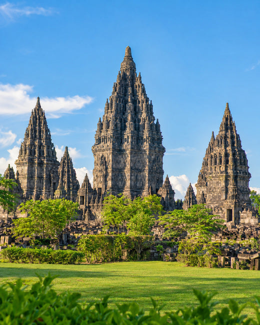 Yogyakarta: steinerne Tempeltürme von Prambanan mit grüner Rasenfläche unter hellem Morgenhimmel
